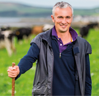 dairy farmer in field with cows behind him