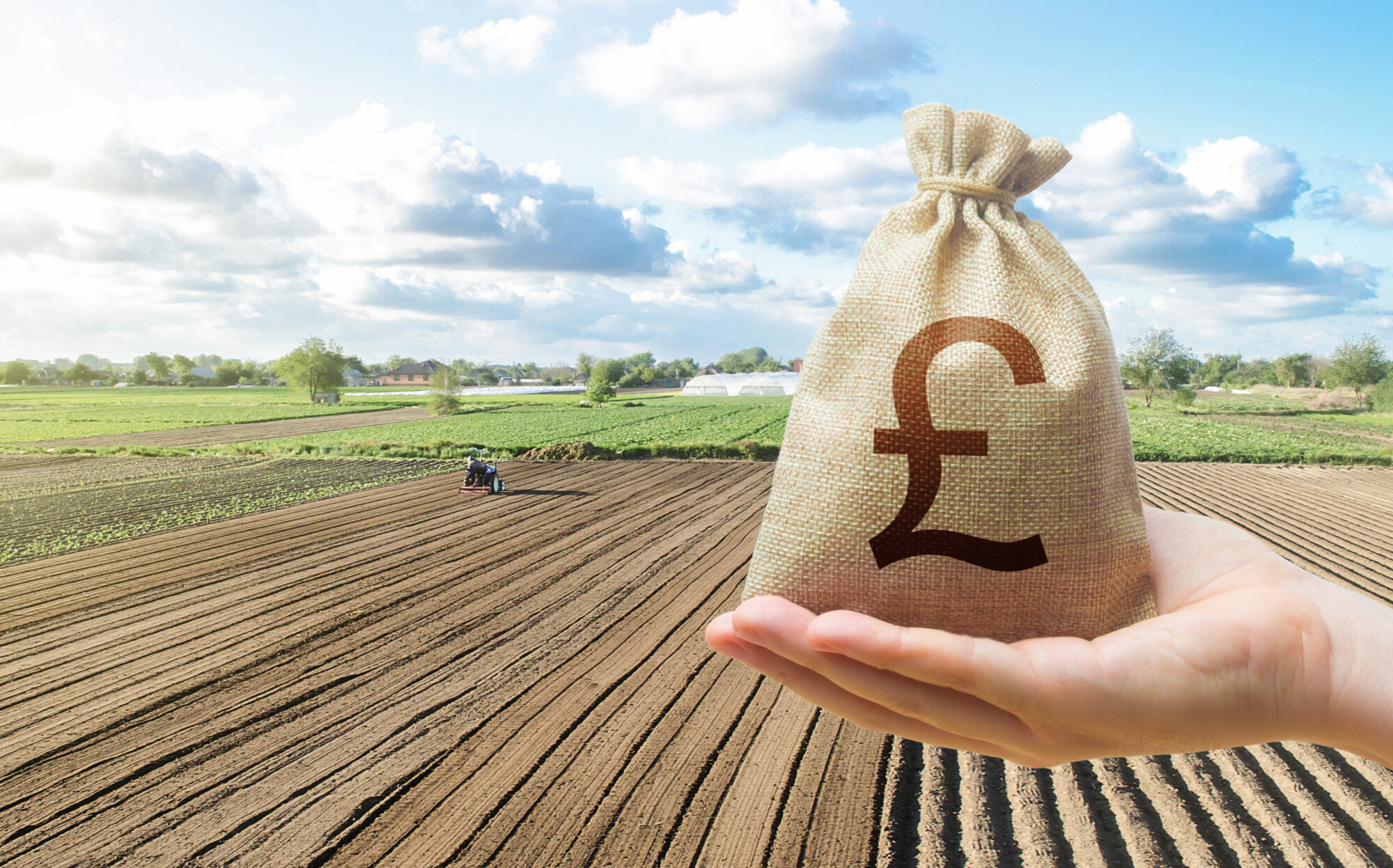 Hand with british pound sterling and a farmer on a tractor works on farm field. Financial support, subsidies for agriculture.