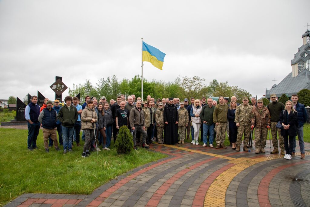 Group of volunteers standing with Ukrainian flag, celebrating 100 4x4s to the army.