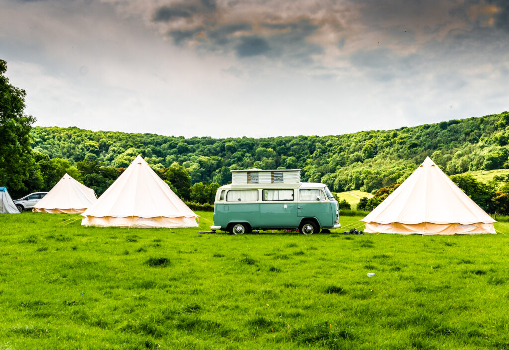 Three yurts surrounding a caper van in a field.