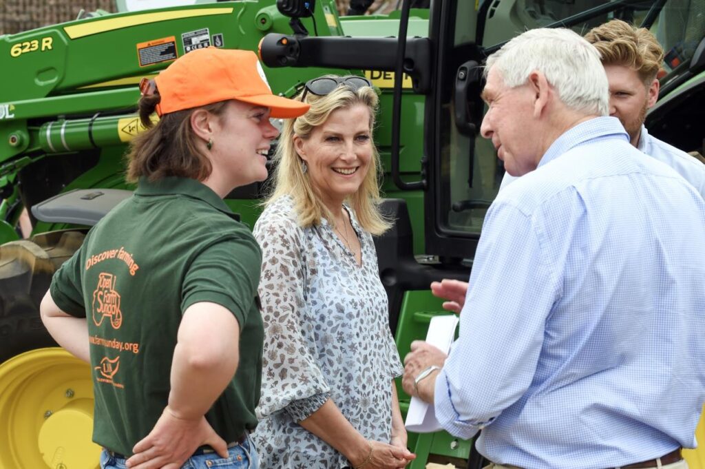 HRH The Duchess of Edinburgh meeting a visitor at Hampton Estate Farms on Leaf Open Farm Sunday, with farmer Molly Biddell, standing in front of a John Deere tractor.