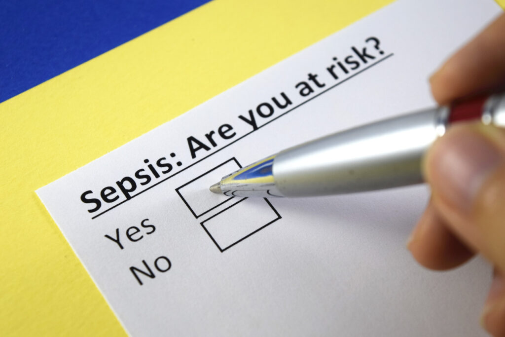 Form reading 'Sepsis: Are you at risk?' with a yes and no tick box. A person's hand holding a pen is shown hovering over the yes tick box 