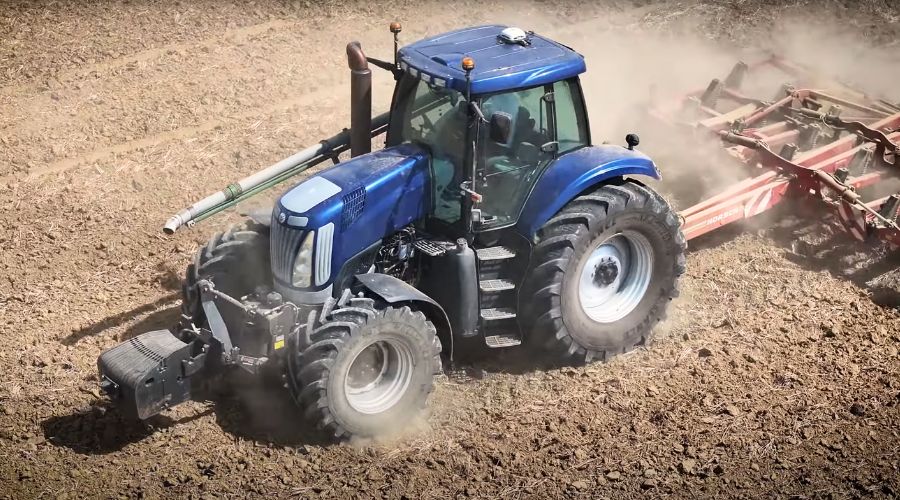 New Holland T7 tractor with Alliance Tyres ploughing barren field. 