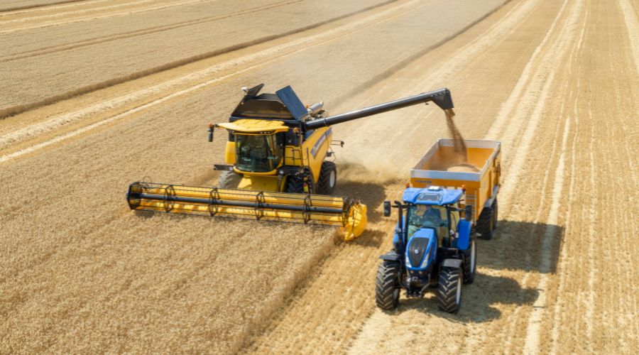 New Holland CH7.70 Combine harvesting a field beside blue tractor