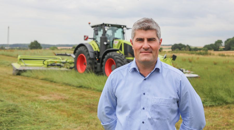 Claas UK forage products specialist, Dean Cottey standing in front of Disco 9700 RC Auto Swather mower-conditioner