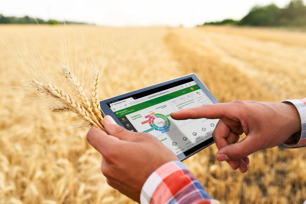 close up of farmer's hands holding a tablet with graphs on it, with a wheat field in the background 