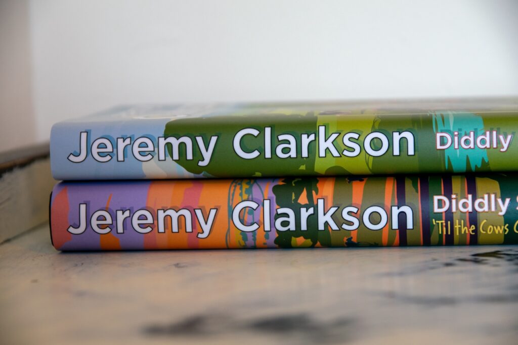 Two Jeremy Clarkson books stacked horizontally on a white marble surface 