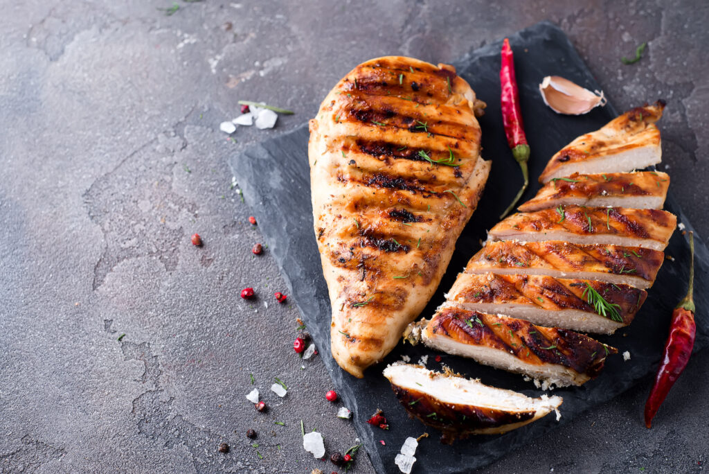 whole and sliced chicken breast with spices on a stone board