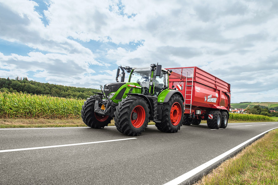 Fendt 728 Vario tractor being driven on the road pulling a trailer 