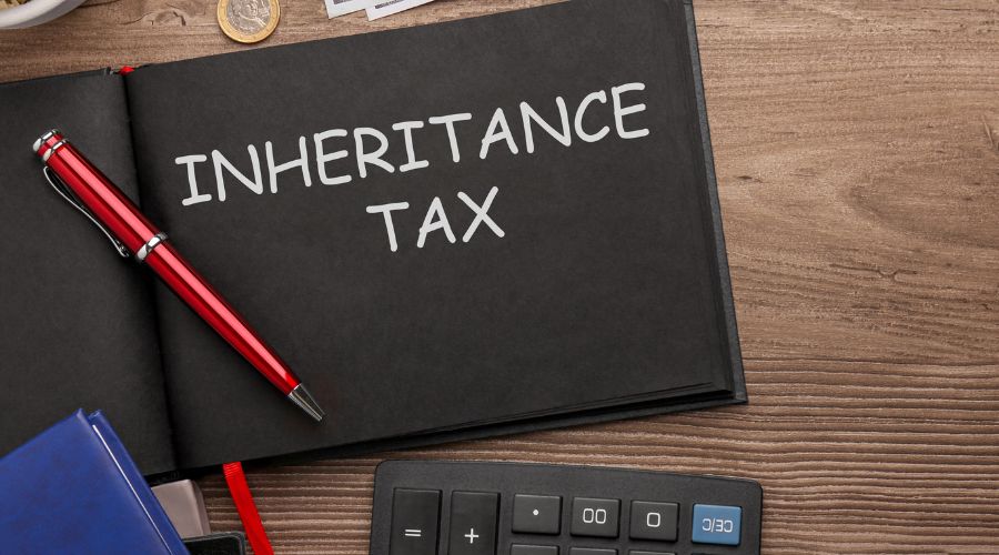 inheritance tax written on a blackboard with a pen and calculator nearby on wooden desk