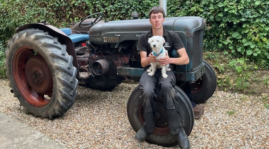 billy kitcher standing in front of his 1954 fordson major tractor, holding a white dog