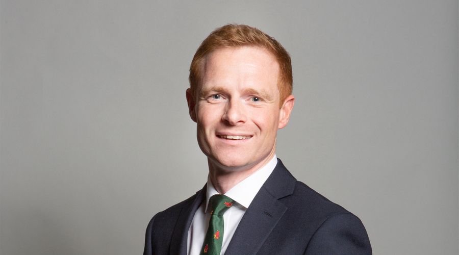 robbie Moore mp in a suit against a grey background