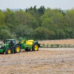 John Deere tractor trailing a sprayer in a field